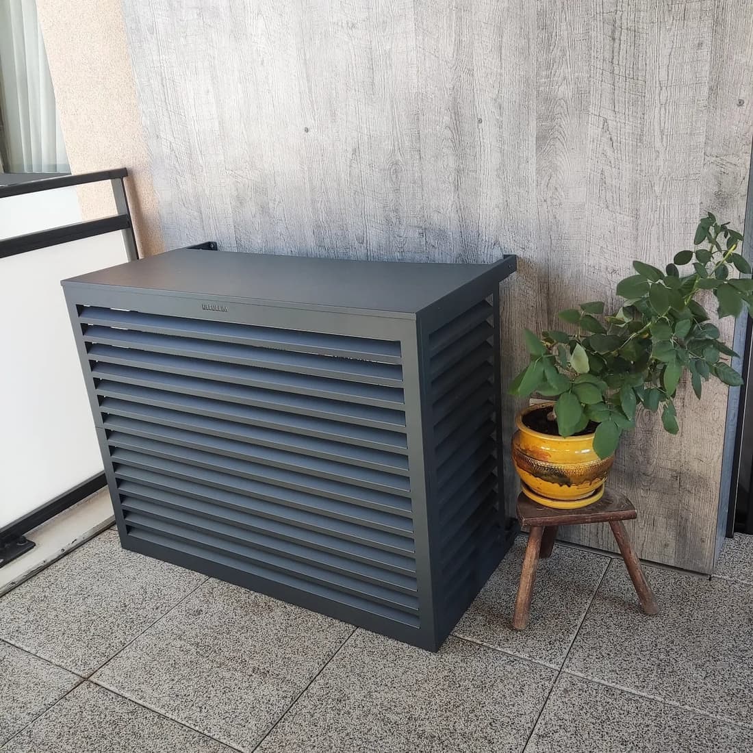 Cache groupe à lamelles gris anthracite habillant l'unité extérieure sur une terrasse en bois