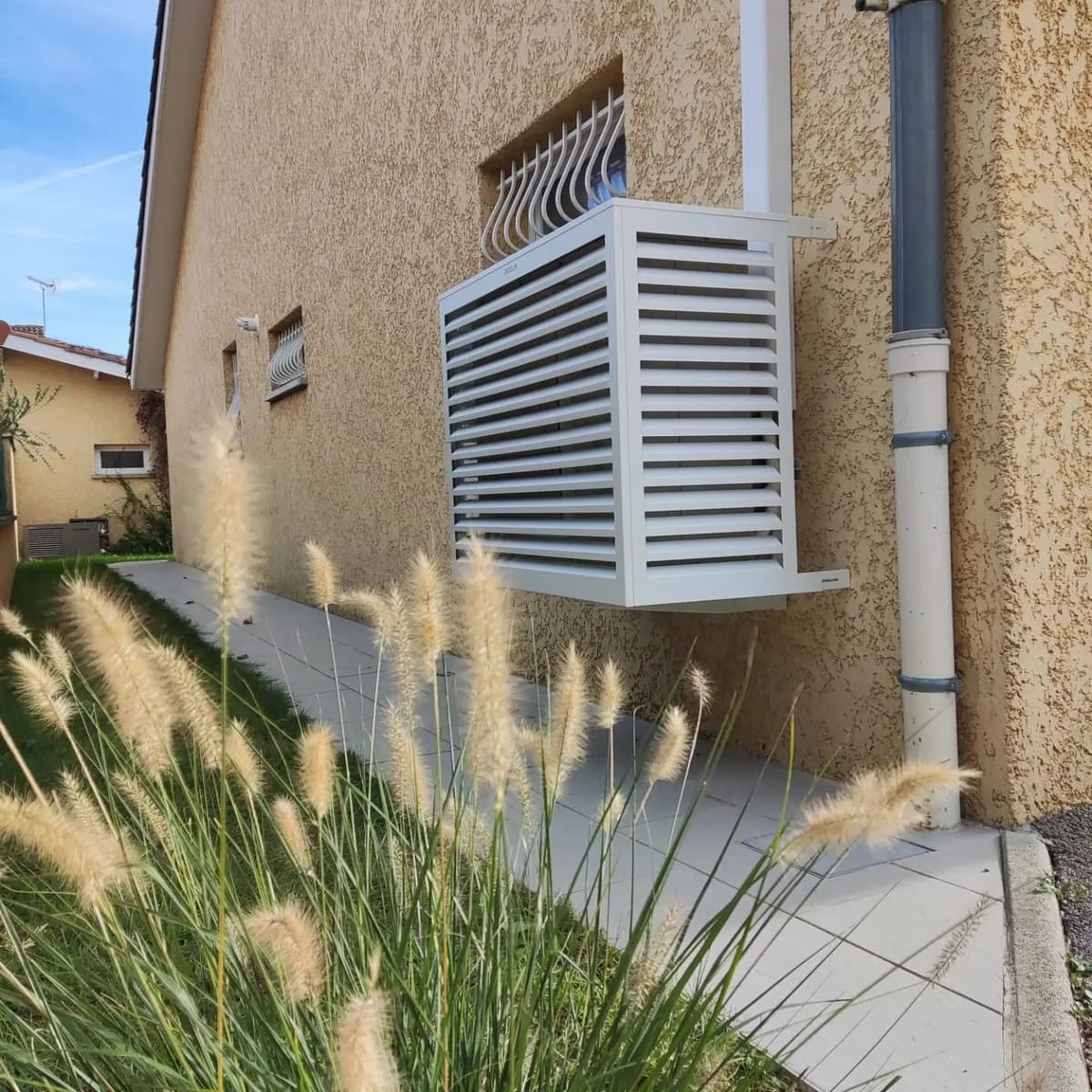 Groupe extérieur de pompe à chaleur habillé d'un cache à lamelles blanc en façade