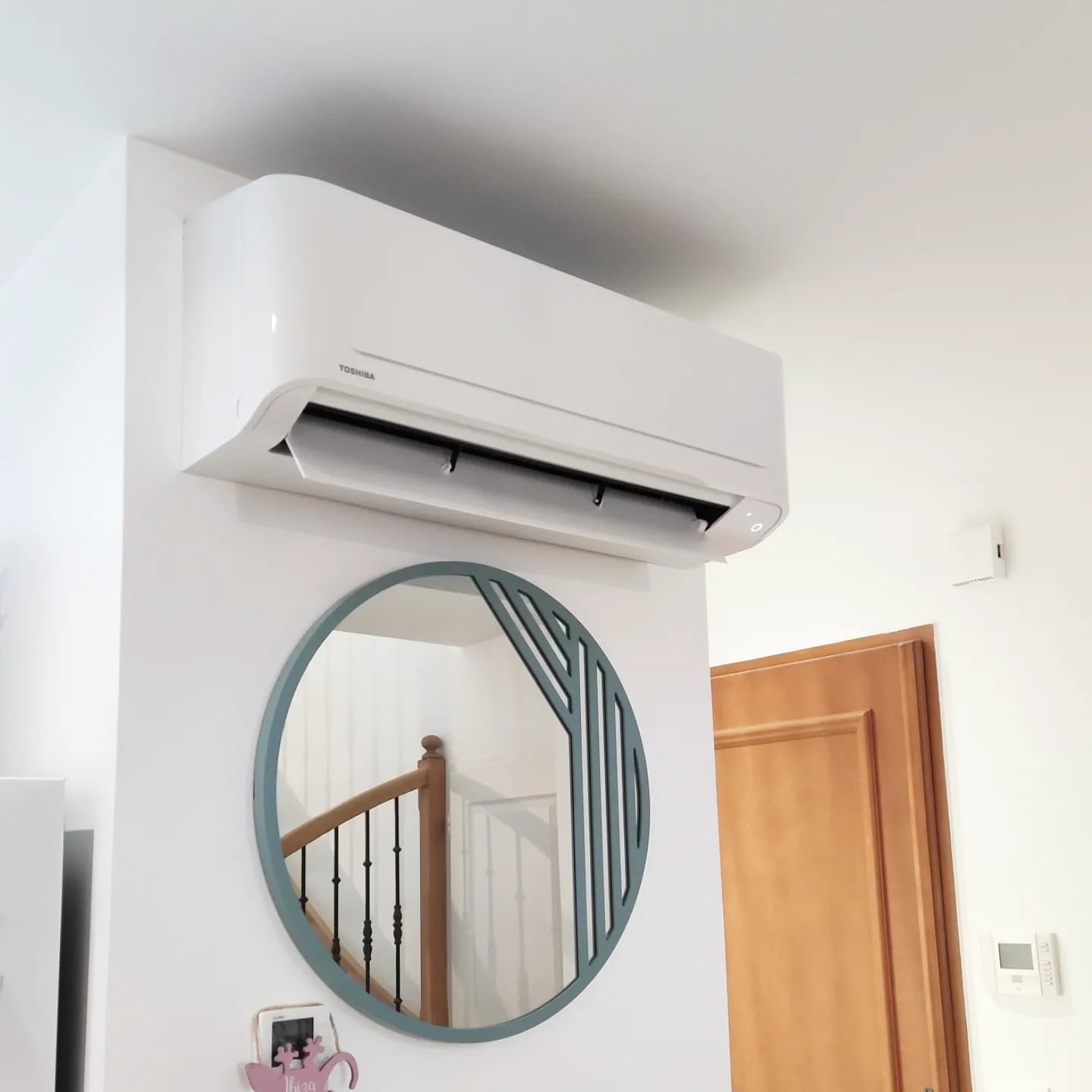 Climatiseur mural Toshiba installé dans une entrée de maison à Meyzieu, au-dessus d'un miroir décoratif